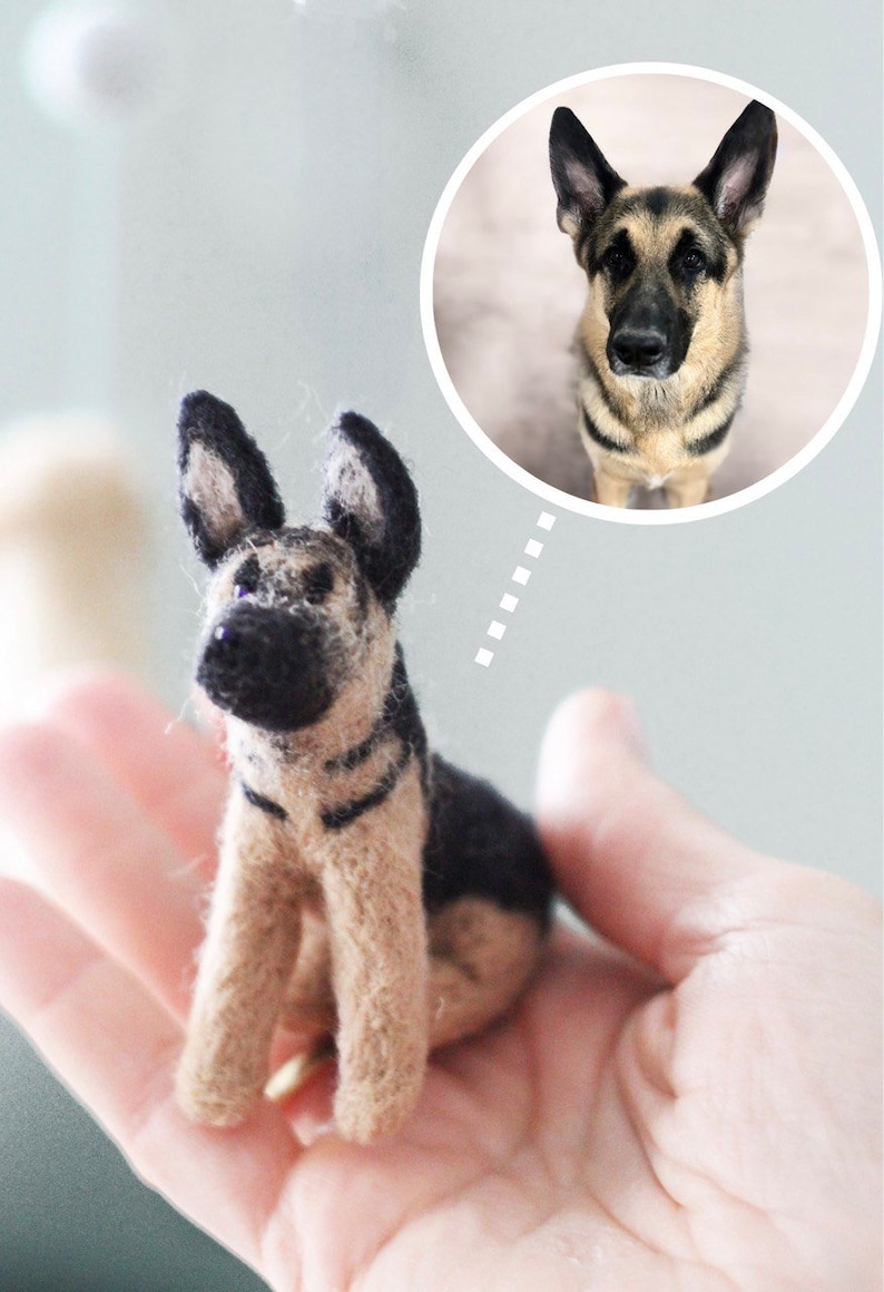 May include: A small, hand-felted German Shepherd dog figurine. The figurine is brown and black with a realistic appearance. It is being held in a person's hand.