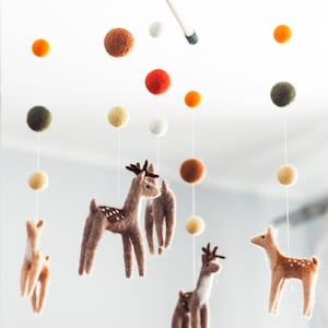 May include: A wooden mobile with felt deer and colorful balls hanging from it. The mobile is suspended from the ceiling.