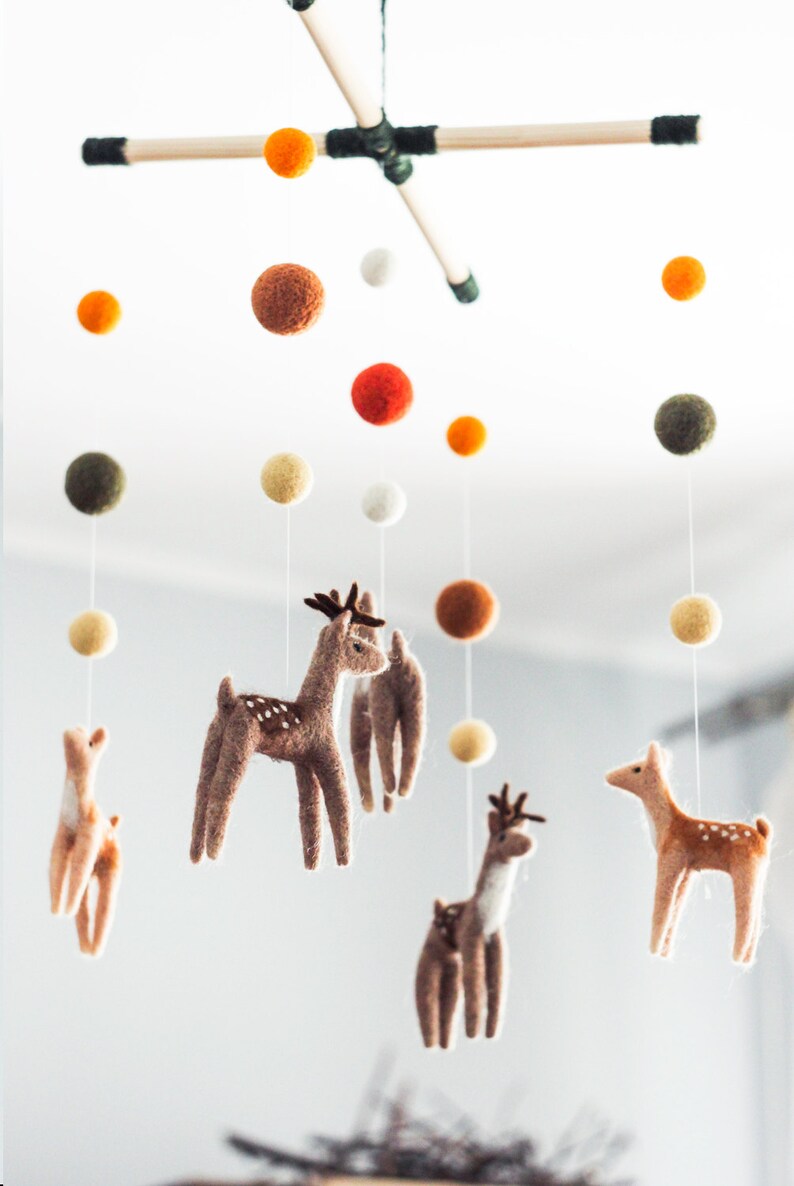 May include: A wooden mobile with felt deer and colorful balls hanging from it. The mobile is suspended from the ceiling.