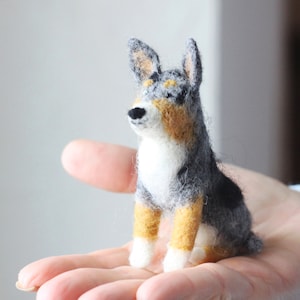 May include: A small, hand-felted dog figurine with black, gray, and tan wool. The dog is sitting upright with its head tilted up.