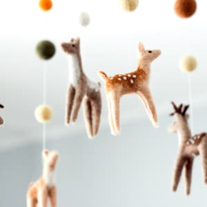 May include: A felt baby mobile with brown and white deer, green and brown balls, and cream colored balls.