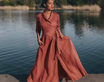 May include: A rust-colored wrap dress with a flowing skirt and three-quarter sleeves. The dress is tied at the waist with a matching belt. The model is standing on a metal dock near a body of water.