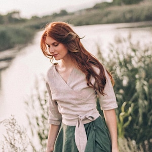 Könnte beinhalten: Eine Frau trägt ein hellbraunes Leinen-Wickeltop mit einem langen, fließenden grünen Leinenrock. Das Oberteil ist mit einer passenden Schärpe in der Taille gebunden. Der Rock ist in der Taille gerafft und reicht bis zu den Knöcheln.