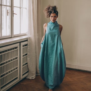 Bring avant-garde and sophistication with this sleeveless maxi dress that is made of 100% linen. It has an asymmetric front with a cowl neckline and a ruched back that could be adjusted. With side pockets and added volume on the sides