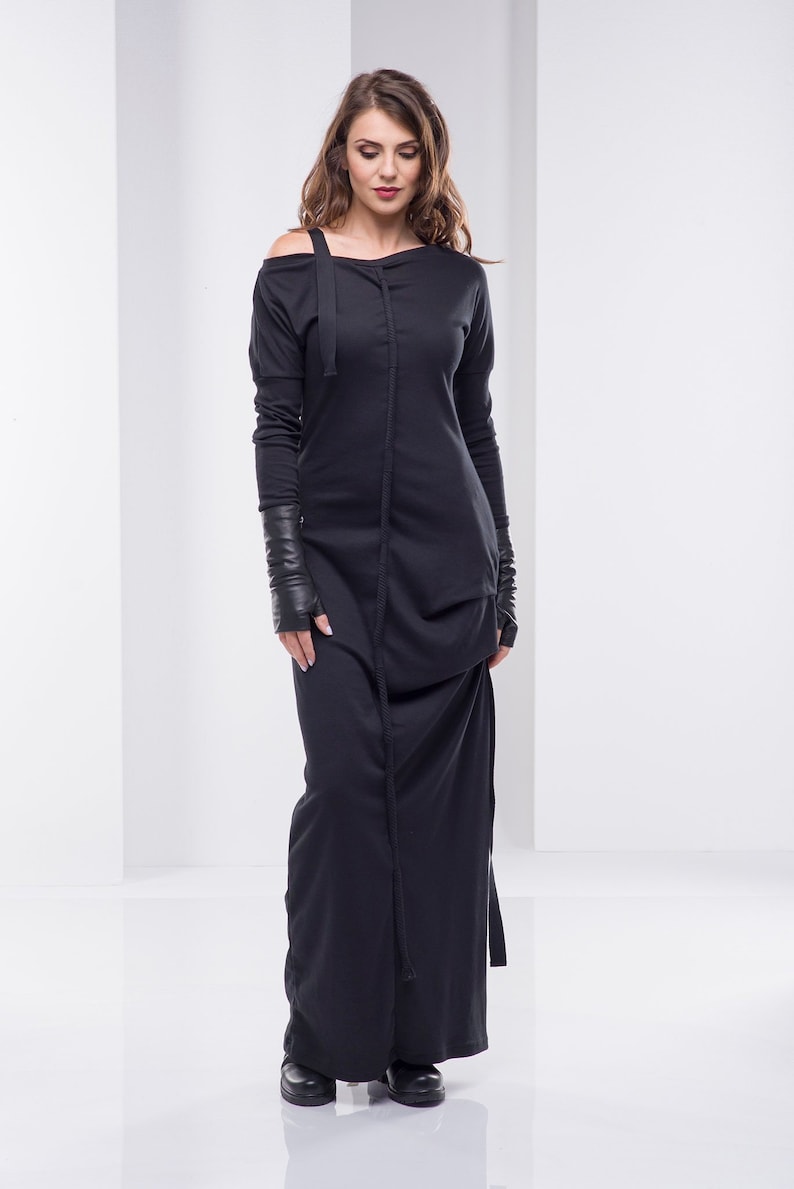 May include: A black long-sleeved dress with a cowl neck and a long, flowing skirt. The dress has a unique design with a seam down the front and a tie at the waist.