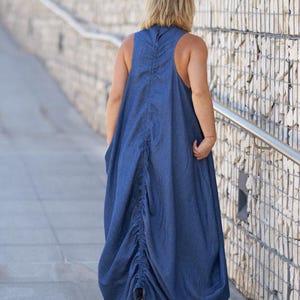 Puede incluir: Una mujer lleva un vestido largo de mezclilla fluido con la espalda fruncida. El vestido es de color azul oscuro y tiene un corte relajado y casual.