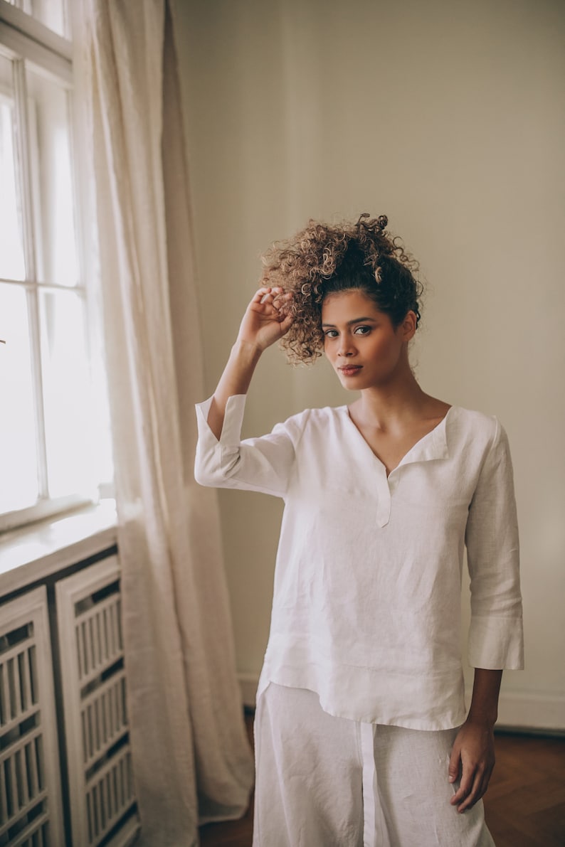 May include: White linen top and matching pants. The top has a V-neck and three-quarter sleeves with a split cuff. The pants are wide-legged. The outfit is made of a lightweight, breathable fabric, perfect for warm weather.