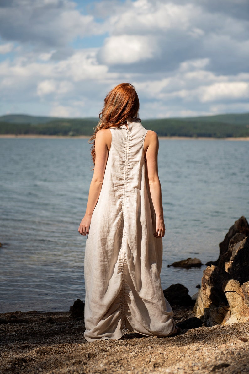 Bring avant-garde and sophistication with this sleeveless maxi dress that is made of 100% linen. This linen dress has an asymmetric front with a cowl neckline and a ruched back that could be adjusted. With side pockets and added volume on the sides.