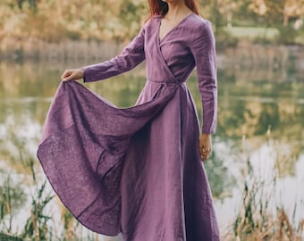 Op de afbeelding: Een wikkeljurk met lange mouwen en een lengte tot op de grond in een effen paarse kleur. Het kledingstuk heeft een V-hals, een aansluitend lijfje met een striksluiting in de taille en een volle, zwierige rok die tot de enkels reikt.