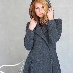 May include: A woman wearing a long, dark gray hooded coat with a shawl collar. The coat has a fitted bodice and a flowing skirt.