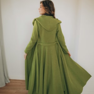 May include: A long, green coat with a hood and a belted waist. The coat is a vibrant shade of green and appears to be made of a soft, textured fabric. The design includes a hood and a flared skirt, creating an elegant silhouette.