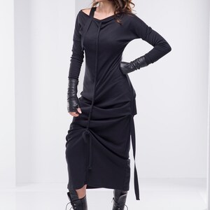 May include: A black long-sleeved dress with a cowl neck and a gathered skirt. The dress is worn with black leather gloves and black combat boots.