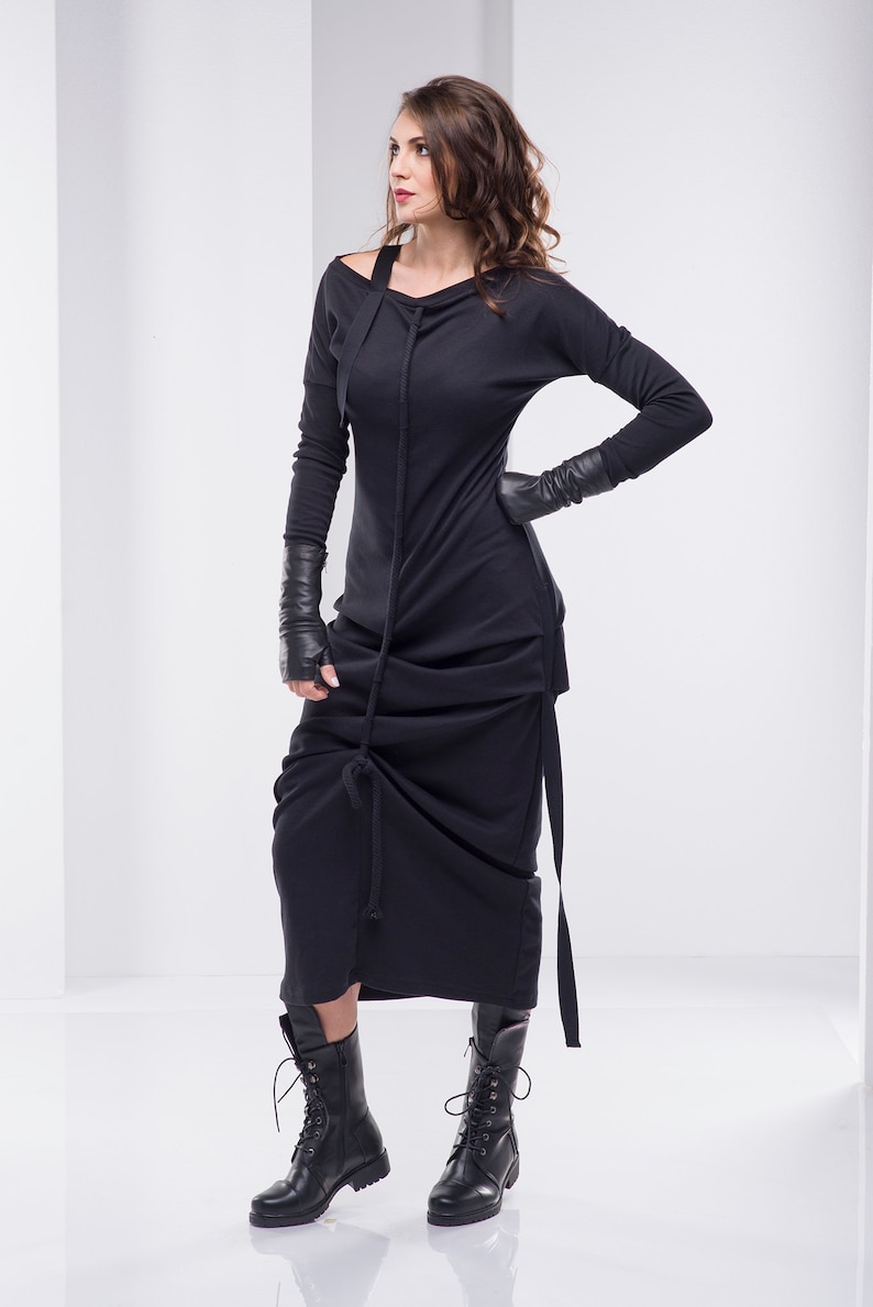 May include: A black long-sleeved dress with a cowl neck and a gathered skirt. The dress is worn with black leather gloves and black combat boots.