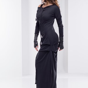 May include: A black long-sleeved dress with a cowl neck and a long skirt. The dress has a unique design with a layered skirt and a cinched waist.
