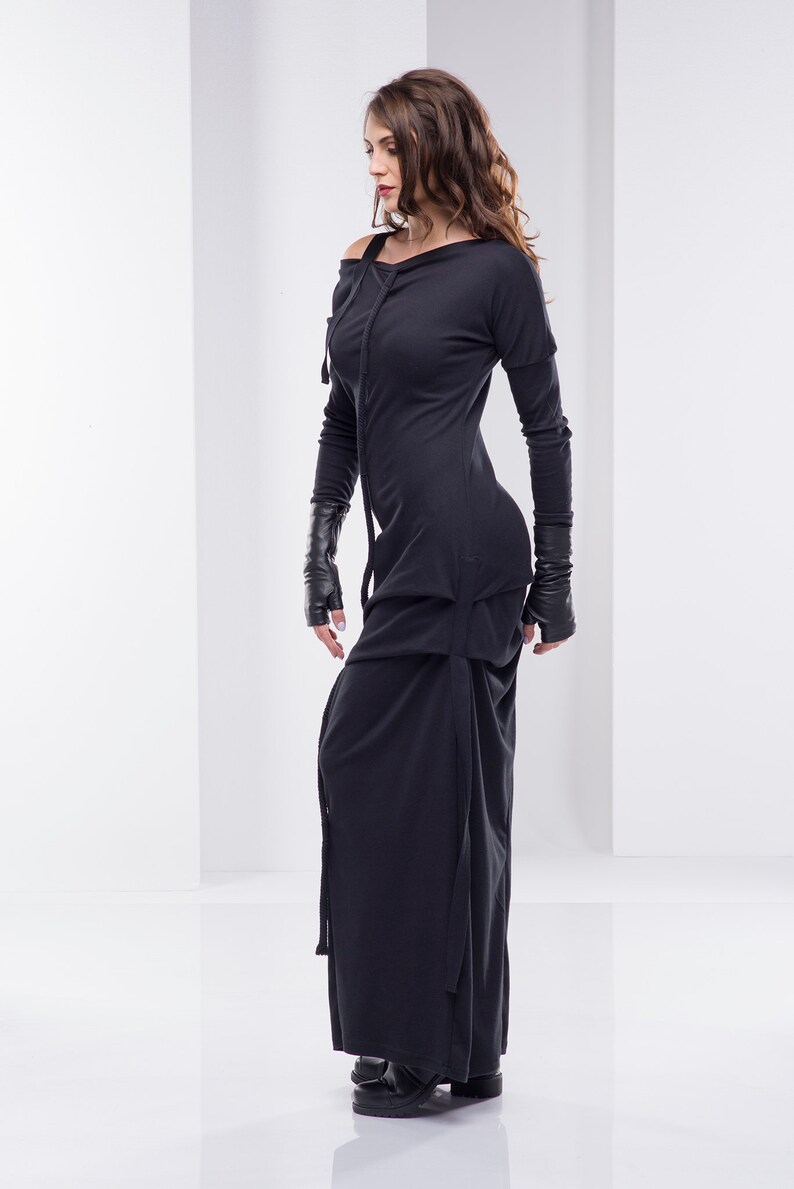 May include: A black long-sleeved dress with a cowl neck and a long skirt. The dress has a unique design with a layered skirt and a cinched waist.