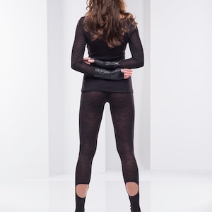 May include: A woman wearing black leggings with cutouts at the ankles, standing in front of a white background.
