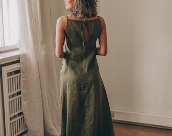 May include: A floor-length olive green linen dress featuring thin spaghetti straps and a keyhole cutout at the upper back with a tie closure. The garment has a straight neckline and a long, flowing skirt that reaches the floor.
