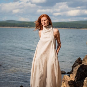 Bring avant-garde and sophistication with this sleeveless maxi dress that is made of 100% linen. This linen dress has an asymmetric front with a cowl neckline and a ruched back that could be adjusted. With side pockets and added volume on the sides.