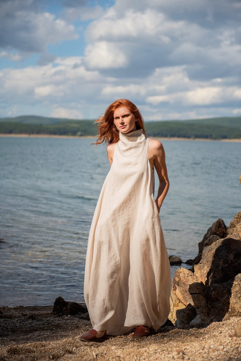 Bring avant-garde and sophistication with this sleeveless maxi dress that is made of 100% linen. This linen dress has an asymmetric front with a cowl neckline and a ruched back that could be adjusted. With side pockets and added volume on the sides.