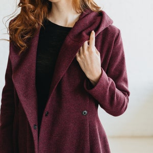 May include: A burgundy hooded coat with a long, flowing design. The coat has a button closure and a relaxed fit.