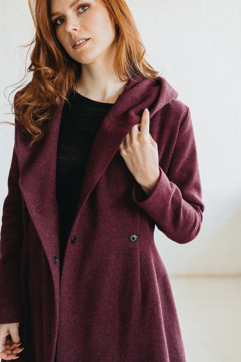May include: A burgundy hooded coat with a long, flowing design. The coat has a button closure and a relaxed fit.