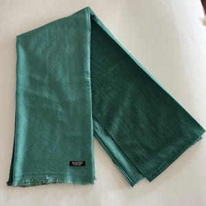May include: A teal green pashmina scarf with a fringed edge. The scarf is folded in half and the tag is visible.