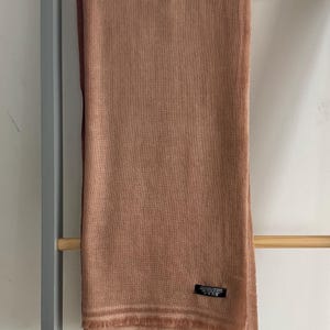 以下が含まれることがあります： フリンジの縁取りが施された、柔らかなブラウンのグラデーションのストール。ストールは軽量素材で作られており、上品な光沢があります。