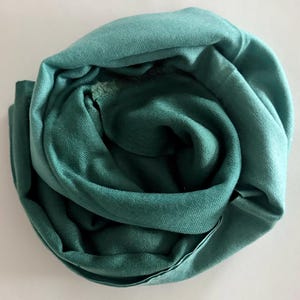 May include: A teal green scarf made of soft fabric, folded into a circular shape.