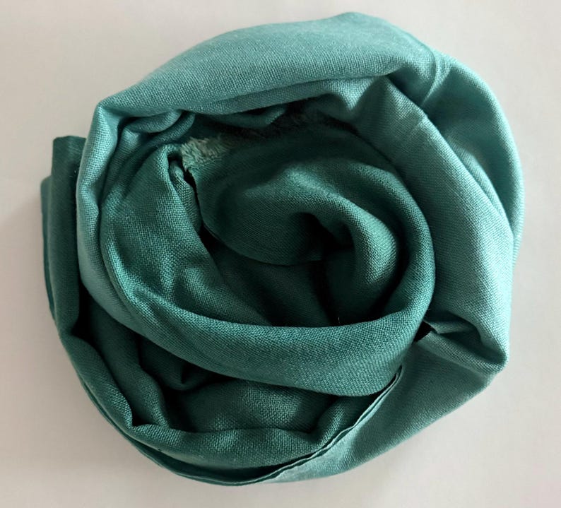 May include: A teal green scarf made of soft fabric, folded into a circular shape.
