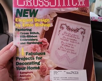 May include: A copy of "Just CrossStitch" magazine from February 1997, featuring a pink cover with the title in a cross-stitch font. The cover advertises "Elegant Design by Emie Bishop" and "14 Fabulous Projects for Decorating Your Home."