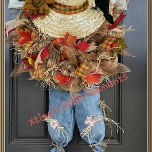 Puede incluir: Una corona de puerta artesanal con tem&aacute;tica de espantap&aacute;jaros. Cuenta con un sombrero de paja con una banda a cuadros, un cuervo negro y un peto vaquero. La corona est&aacute; adornada con follaje oto&ntilde;al, girasoles y malla decorativa.