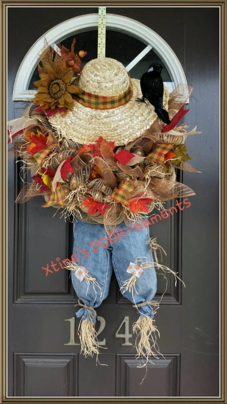 Puede incluir: Una corona de puerta artesanal con tem&aacute;tica de espantap&aacute;jaros. Cuenta con un sombrero de paja con una banda a cuadros, un cuervo negro y un peto vaquero. La corona est&aacute; adornada con follaje oto&ntilde;al, girasoles y malla decorativa.