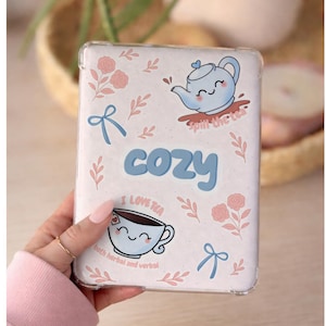 Könnte beinhalten: Eine transparente Handyhülle mit einem gemütlichen Tee-Thema. Die Hülle zeigt eine blaue Teekanne, eine Teetasse, rosa Rosen und das Wort "cozy" in Blau. Die Sätze "I love tea" und "spill the tea" sind ebenfalls enthalten.