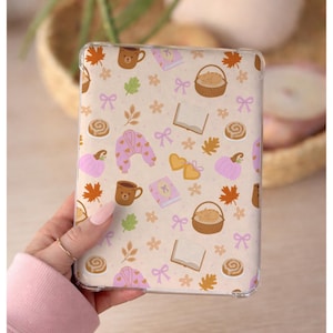 May include: A clear tablet case featuring a repeating pattern on a light beige background. The design includes brown bear mugs, orange maple leaves, pink pumpkins, open books, cinnamon rolls, sleeping cats in baskets, pink robes, and bows.