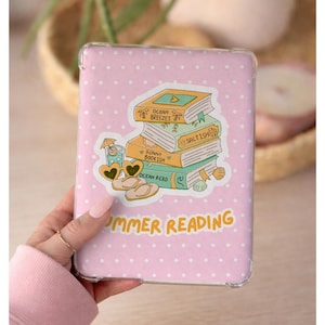 Puede incluir: Una funda rosa para lector de libros electrónicos con un estampado de lunares blancos. La funda presenta una pegatina con una pila de libros, un cóctel y sandalias. El texto "SUMMER READING" está impreso en amarillo.