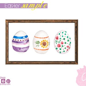 May include: Three watercolor Easter eggs in a brown frame. The eggs are decorated with different patterns: purple and blue stripes with white dots, yellow and orange sunflowers with green leaves, and red and pink flowers with green leaves and green dots.
