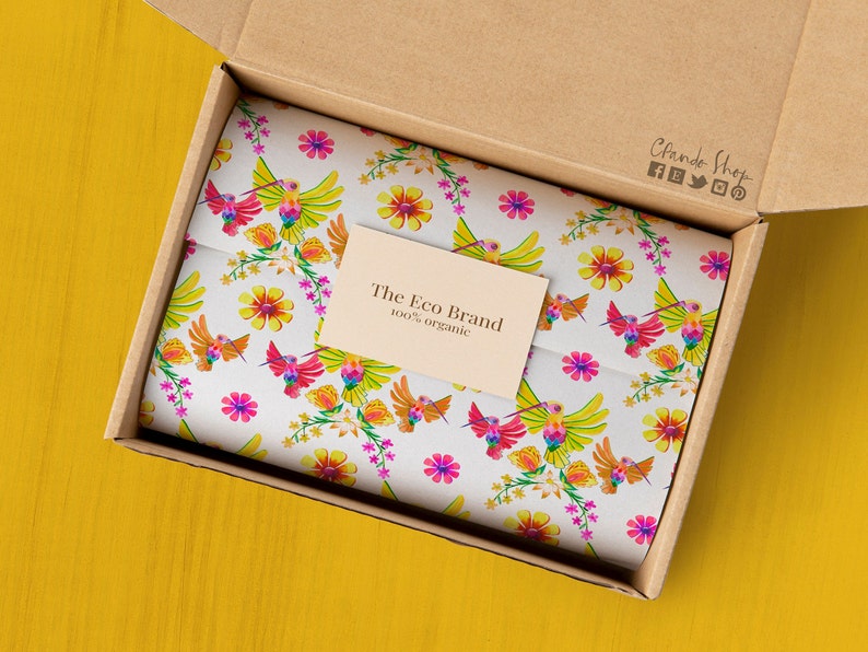 May include: A cardboard box with a white tissue paper lining. The tissue paper has a colorful pattern of hummingbirds and flowers. A small card with the text "The Eco Brand 100% organic" is visible on the tissue paper.