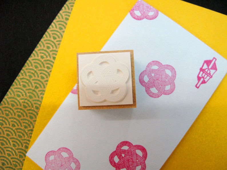 Op de afbeelding: Een witte rubberen stempel met een gedetailleerd bloemenpatroon op een lichtblauwe achtergrond met roze bloemenpatronen. De stempel ligt op een geel oppervlak.