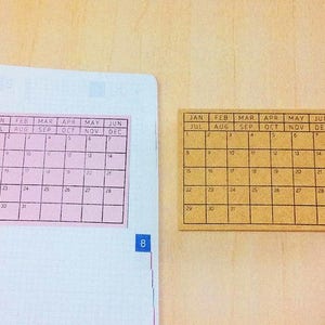 May include: Two calendar stickers, one pink and one brown, with the months of the year and days of the week labeled. The pink sticker has the months July through December, while the brown sticker has the months January through June.