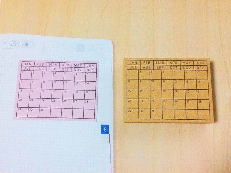 May include: Two calendar stickers, one pink and one brown, with the months of the year and days of the week labeled. The pink sticker has the months July through December, while the brown sticker has the months January through June.