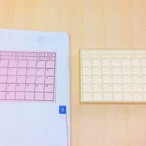 May include: Two calendar stamps, one pink and one white, with the months of the year printed on them. The pink stamp has the numbers 1 through 31 printed in the squares. The white stamp has blank squares.