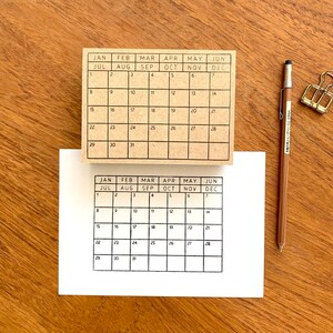 May include: Two brown wooden calendar stamps with black ink. The top stamp has the months January through June and the bottom stamp has the months July through December. Both stamps have the days of the week and numbers 1 through 31.