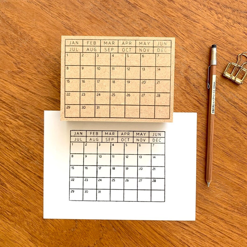 May include: Two brown wooden calendar stamps with black ink. The top stamp has the months January through June and the bottom stamp has the months July through December. Both stamps have the days of the week and numbers 1 through 31.
