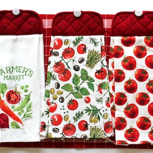 May include: Three red quilted kitchen towels with white cotton tea towels hanging from them. The tea towels have different designs. One has a farmer's market theme with illustrations of vegetables. Another has a tomato and basil design. The third has a tomato design.