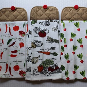 May include: Three kitchen towels with brown quilted tops and red button closures. The towels feature white backgrounds with colorful illustrations of chili peppers, vegetables, and radishes. The chili pepper towel has text labels.