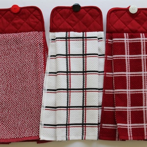 May include: Three red kitchen towels with different patterns. The towels have a red quilted top with a button closure. The patterns include a red and white checkered pattern, a black and white checkered pattern, and a red and white textured pattern.