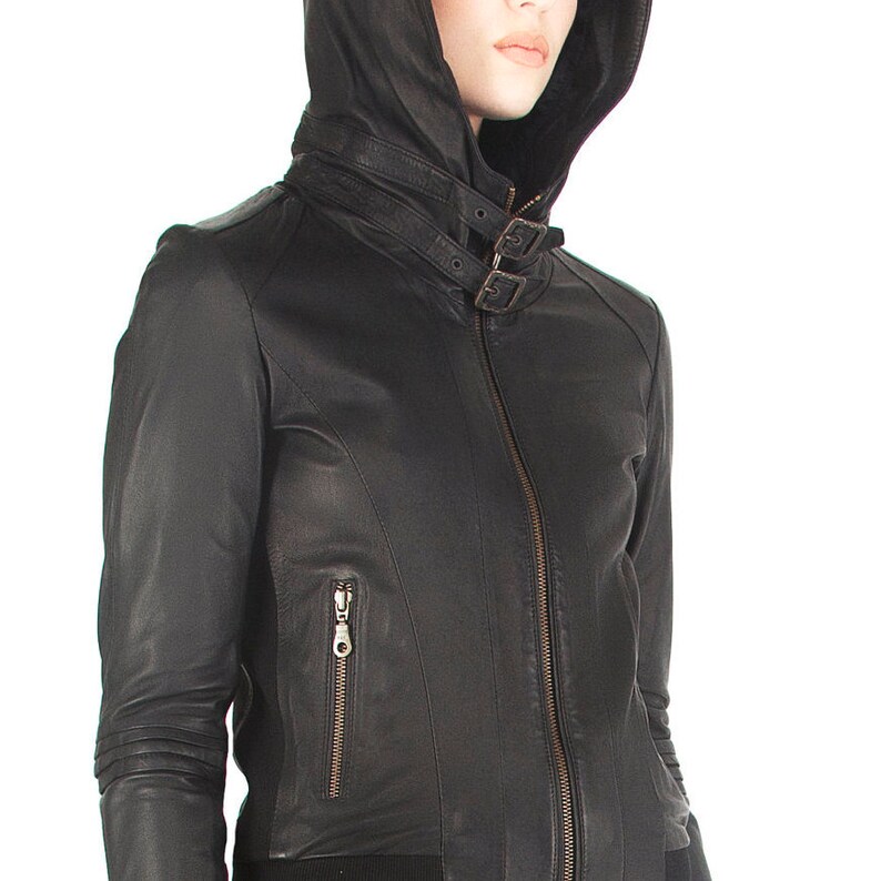 May include: Black leather jacket with a hood and a zipper closure. The jacket has a buckle detail on the collar and a zippered pocket on the left side.