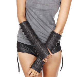 Könnte beinhalten: Schwarze Leder-Armstulpen mit Knopfdetails. Die Armstulpen haben ein geripptes Design und werden an den Armen getragen. Die Handschuhe sind fingerlos und haben einen Knopfverschluss. Ein Modeaccessoire.