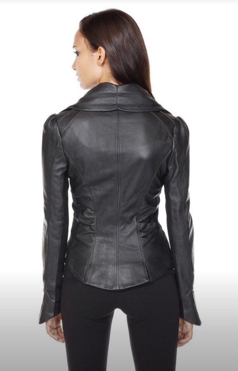 Puede incluir: Chaqueta de cuero negra con corte entallado, con cuello con solapas y mangas largas. La chaqueta tiene cintura entallada y detalles sutiles en los hombros. La modelo lleva pantalones negros. La chaqueta es de cuero.