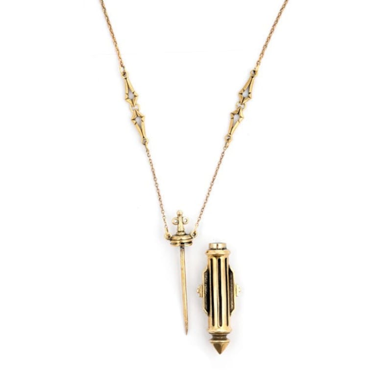May include: A gold chain necklace with a pendant that is a small, ornate sword and a small, ornate tube. The tube has a pointed end and a decorative top.